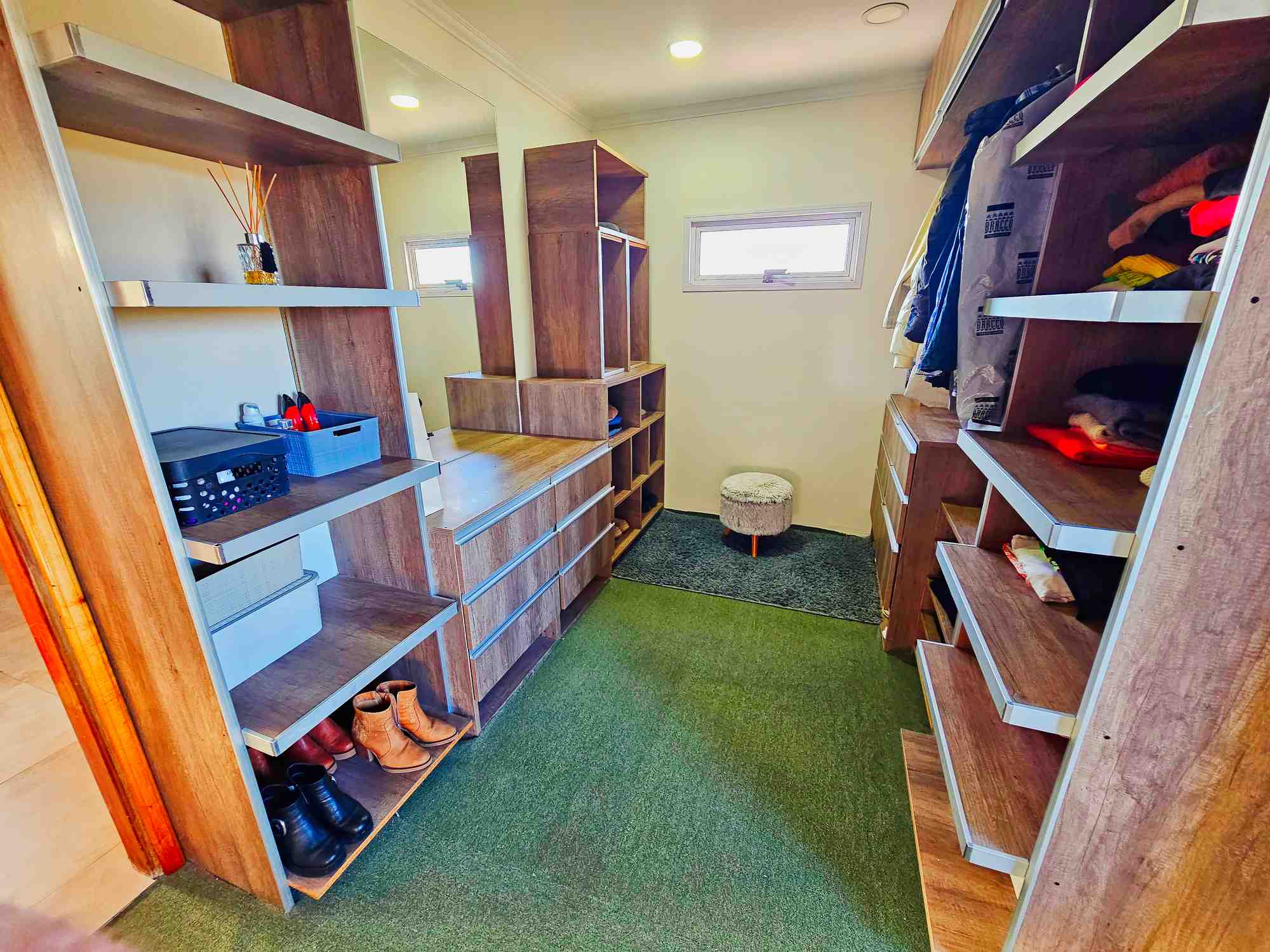Vestidor con estanterías de madera, zapatos y ropa colgada en casa de lujo