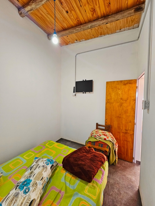 Dormitorio con cama colorida, manta marrón y televisor montado en la pared